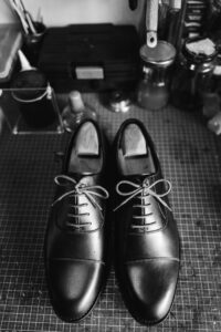 A classic black and white photograph highlighting elegant leather shoes on a workbench.