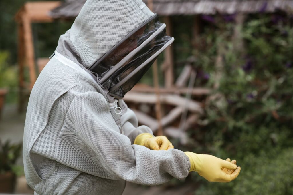 Crop male beekeeper in protective uniform and gloves standing in apiary while preparing for work