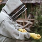 Crop male beekeeper in protective uniform and gloves standing in apiary while preparing for work