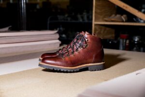 Close-up of brown leather boots with a rugged sole on a workshop table, showcasing craftsmanship.